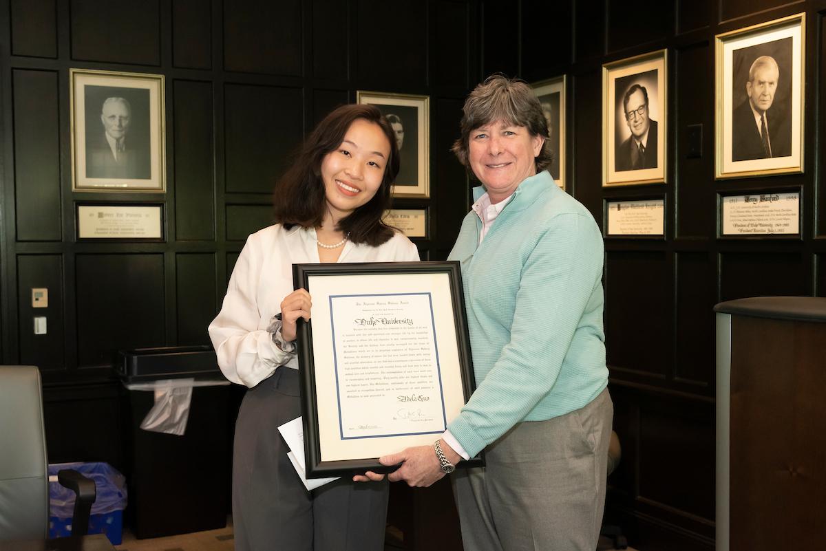 Adela Guo holds framed plaque with Jennifer Francis